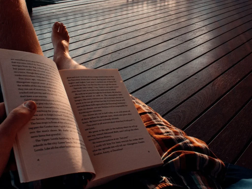 Person reading a book on a wooden deck in the sun